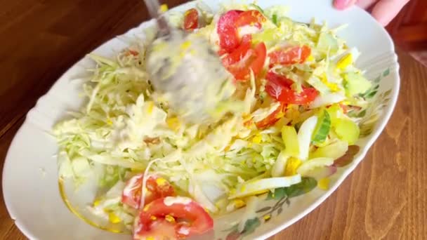 Mixing salad with fresh vegetables, tomatoes, peppers, cucumbers, cabbage, and eggs using a spoon. - Felvétel, videó