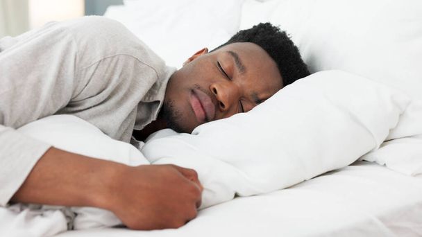 Slapen, ontspannen en dromen voor een zwarte man thuis in bed op een weekend ochtend. Moe, slapen en dromen in de slaapkamer alleen. Ontspannen, rust en comfort met hoofd op kussen voor slaperige tijd in lichte kamer - Foto, afbeelding