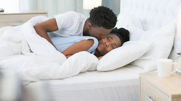 Kiss, bed and couple sleeping together in bedroom or waking up on weekend morning for luxury furniture, hotel or hospitality. Black people, woman or husband love, care and marriage for valentines day. - Valokuva, kuva