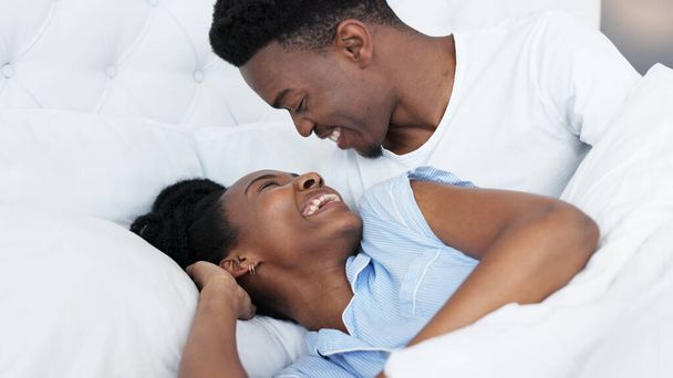 Happy black couple in bedroom kiss and smile for love, romance and intimacy at house or home in morning. Young, happiness and kissing black woman and man or romantic black people dating bond together. - Фото, изображение