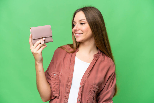 Молода блондинка тримає гаманець над ізольованим ключовим фоном хромосоми з щасливим виразом
 - Фото, зображення