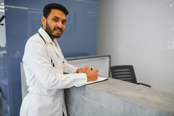 Portrait of happy friendly male Indian latin doctor medical worker wearing white coat with stethoscope around neck standing in modern private clinic looking at camera. Medical healthcare concept. - Foto, Bild