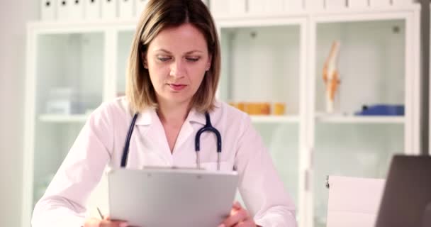 El médico examina los documentos médicos en el lugar de trabajo en la clínica. Diagnósticos médicos de salud - Metraje, vídeo