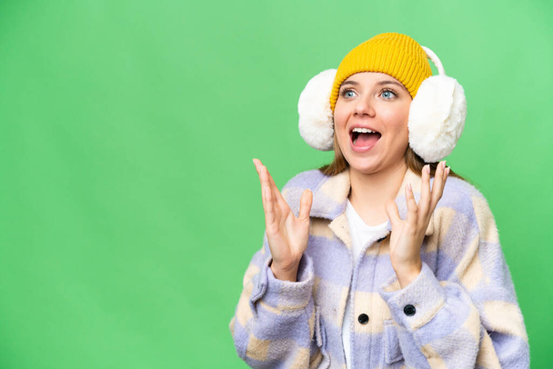 Young blonde woman wearing winter muffs over isolated chroma key background with surprise facial expression - Фото, изображение