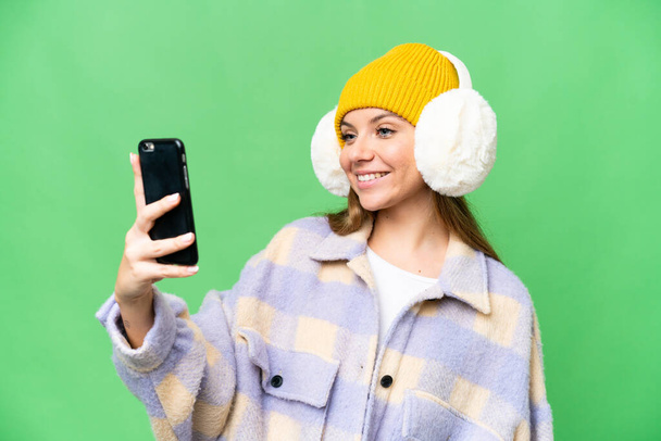 Jeune femme blonde portant des manchons d'hiver sur fond isolé chroma clé faire un selfie - Photo, image