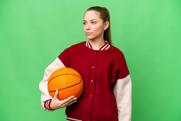 fiatal szőke nő kosárlabda felett elszigetelt chroma kulcs háttér nézi az oldalon - Fotó, kép