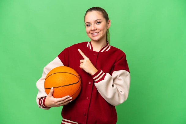 Молодая блондинка, играющая в баскетбол над изолированным цветовым фоном, указывая на сторону, чтобы представить продукт - Фото, изображение