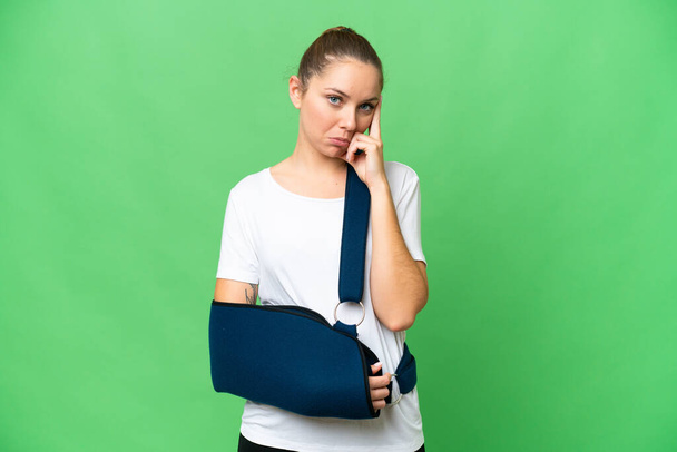 Young blonde woman with broken arm and wearing a sling over isolated chroma key background thinking an idea - Foto, Imagem