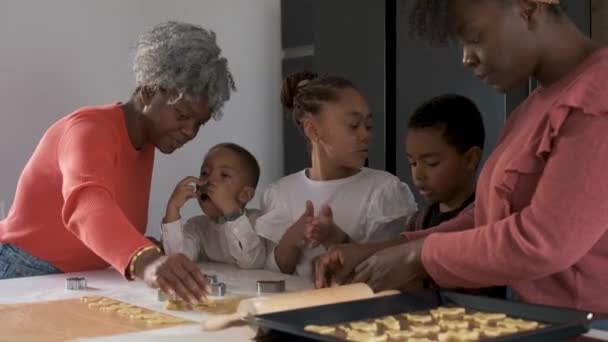 African family cutting cookie shapes in a cookie dough in the kitchen. Horizontal extended family. - Video