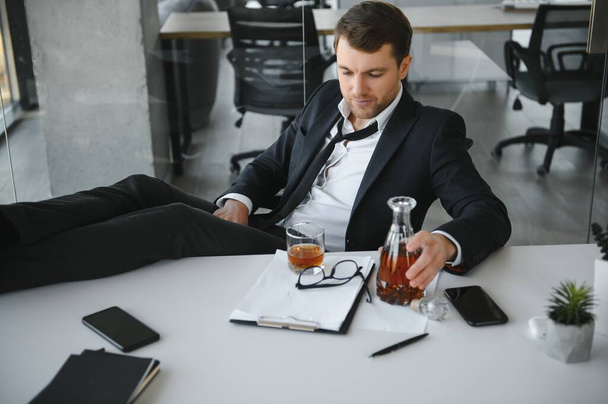 Young businessman drinking from stress. - 写真・画像