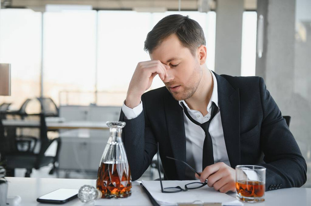 Alcoholism at work. Tired employee drinking alcohol at workplace, can not handle stress - Zdjęcie, obraz