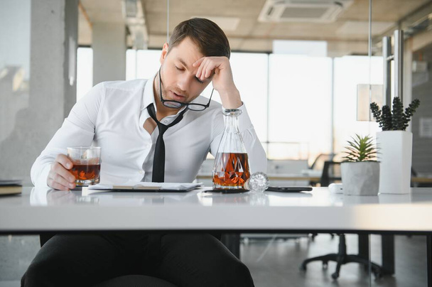 Alcoholism at work. Tired employee drinking alcohol at workplace, can not handle stress - Фото, зображення