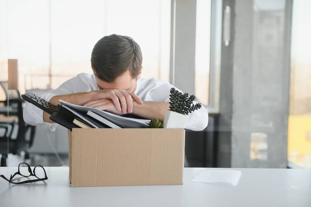 Sad Fired. Let Go Office Worker Packs His Belongings into Cardboard Box and Leaves Office. Workforce Reduction, Downsizing, Reorganization, Restructuring, Outsourcing. Mass Unemployment Market Crisis. - Valokuva, kuva