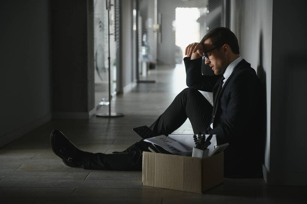 Sad fired businessman sitting outside meeting room after being dismissed - 写真・画像