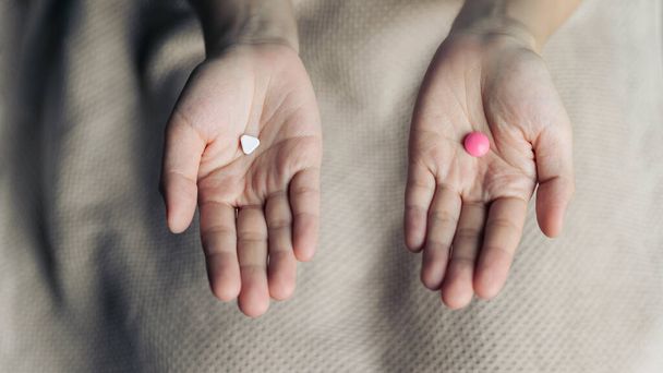 Female hands hold and offer two choice medicine pills capsule for chosen. White and pink candy or meds compare to choose from. Concept indecisiveness or decision making. - Zdjęcie, obraz
