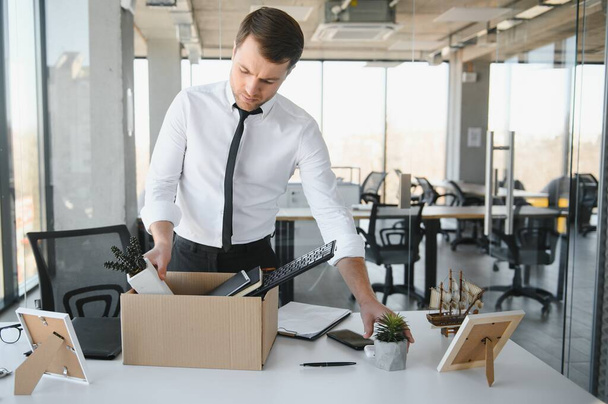 Sad Fired. Let Go Office Worker Packs His Belongings into Cardboard Box and Leaves Office. Workforce Reduction, Downsizing, Reorganization, Restructuring, Outsourcing. Mass Unemployment Market Crisis. - 写真・画像