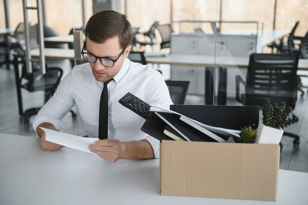 Young handsome businessman in light modern office with carton box. Last day at work. Upset office worker is fired - Foto, imagen