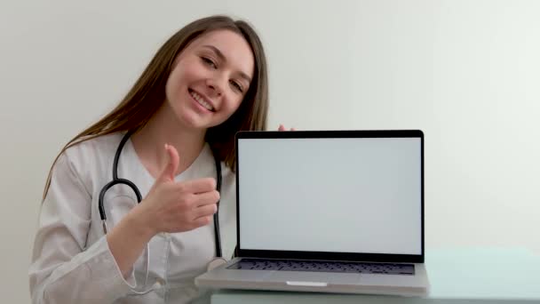 terapeuta pediátrico médico mostrando pulgar hacia arriba fondo blanco en el ordenador monitor portátil sonrisa espacio para ad dentista cardiólogo endocrinólogo tratamiento ayudar a las personas asistencia mutua medicina - Imágenes, Vídeo