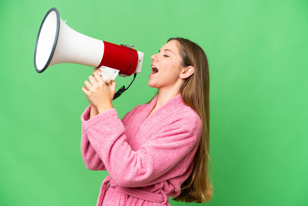 Young woman in a bathrobe over isolated chroma key background shouting through a megaphone - Fotografie, Obrázek