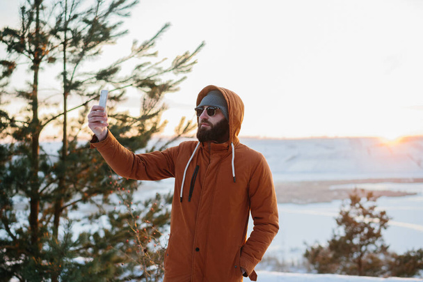 Un excursionista disfruta de la puesta de sol en las montañas de invierno y toma una foto en su teléfono. - Foto, imagen