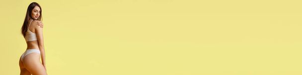 Hübsches junges Mädchen posiert in Baumwollunterwäsche über gelbem Studiohintergrund. Gewichtsverlust. Konzept der Schönheit, Körper- und Hautpflege, Fitness, Gesundheit, Wellness, Kosmetik. Horizontales Banner für Anzeige, Text - Foto, Bild