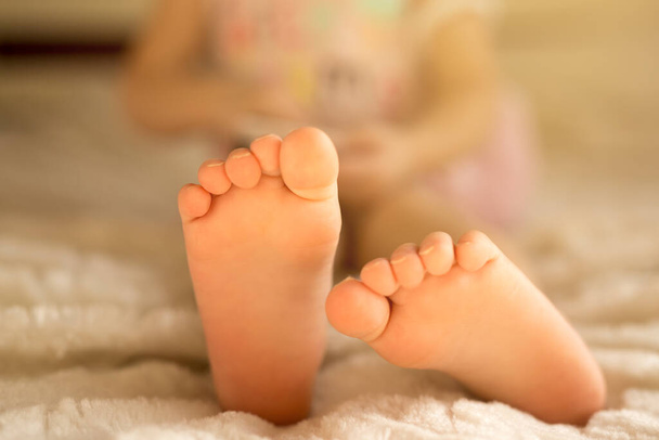 Sen, odpoczynek, dzieciństwo, nogi. Gołe stopy dziecka na dorosłym łóżku. Skupienie selektywne - niewyraźne tło - Zdjęcie, obraz