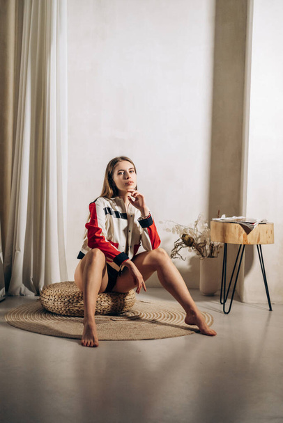 Blonde with long hair and jacket sits on the floor. Girl posing for a photo shoot - Fotó, kép