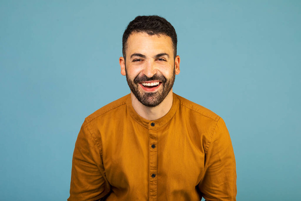 Cheerful man smiling happily at camera, posing isolated over blue studio background, free space. People, youth, emotions concept - Фото, изображение