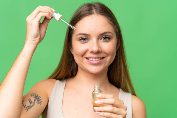 Young blonde woman over isolated chroma key background holding a serum while smiling. Close up portrait - Foto, Imagem