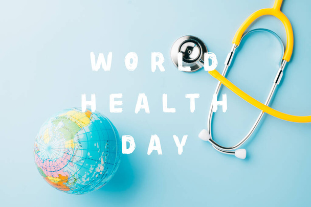 Egészségügyi Világnap. Felülnézet sárga orvos sztetoszkóp csomagolva a világ körül elszigetelt pasztell kék háttér másolási hely szöveg, Globális egészségügyi, Egészségügyi és orvosi koncepció - Fotó, kép
