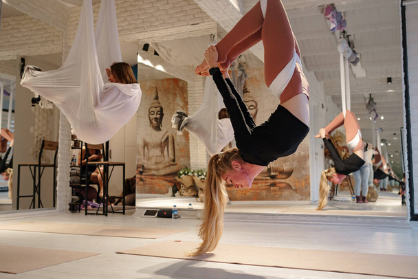 Workshop für Luft-Yoga und Stretching im Yoga-Studio. Frauen praktizieren mit Hängematte unterschiedliches Antigravitations-Yoga. Balance zwischen Geist und Körper, Anstrengung einer Person und Leistungskonzept - Foto, Bild