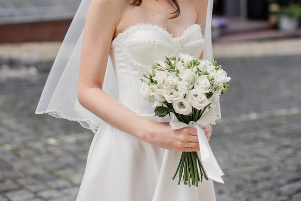 bride in a white dress with a wedding bouquet on a city street - Foto, Imagen
