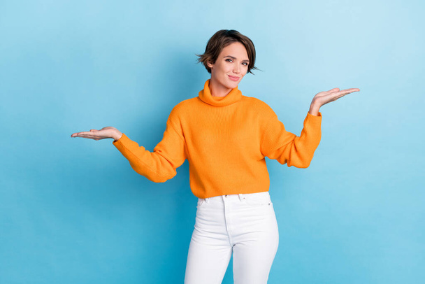 Photo portrait of lovely young lady raise hands palms compare empty space dressed stylish orange outfit isolated on blue color background. - Фото, зображення