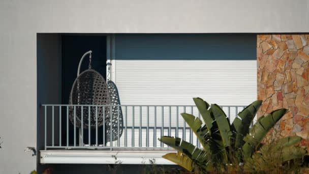 Балкон з розмахуючим кріслом, покритим закритими жалюзі, оточений пишною рослинністю і яскравим сонячним світлом, без людей в кадрі. Зйомки фільму в Португалії - Кадри, відео