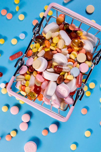 Különböző kapszulák, tabletták és gyógyszerek egy bevásárlókocsiban, kék alapon. Egészségügy, kezelés. A gyógyszervásárlás és a gyógyszervásárlás fogalma. - Fotó, kép