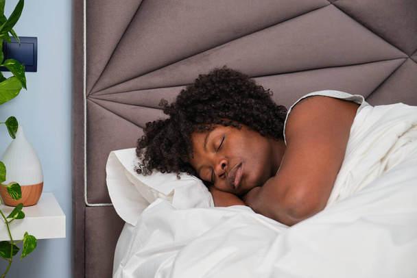 Jeune femme africaine dormant sur des draps blancs au lit. Repos endormi. - Photo, image