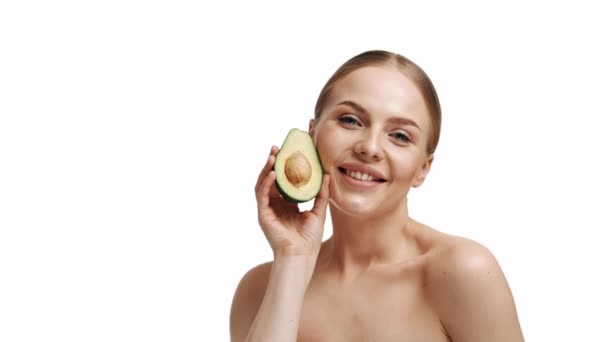 Smiling woman with half an avocado. Photo of attractive woman with perfect makeup on white background. Beauty and Skin care concept. - Záběry, video