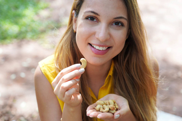 Natural healthy girl picking cashew nuts from her hand in the park. Looks st camera. - Photo, Image