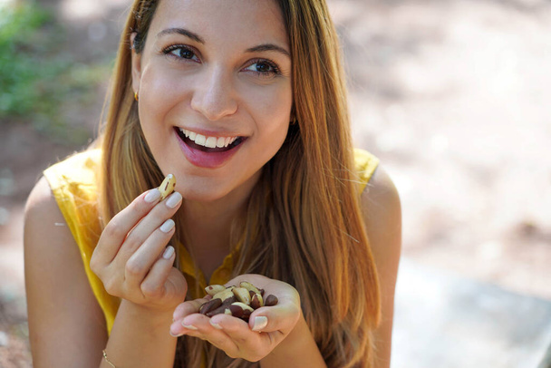 Close-up of attractive healthy woman eating Brazil nuts outoor. Looks to the side. - Photo, Image