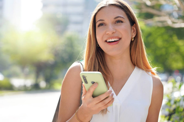 Close-up of laughing casual woman looking away holding her mobile phone outdoors - Foto, Imagem
