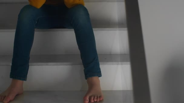 The camera slowly moves from the feet to the face, revealing a teenage boy wearing a yellow sweater, sitting on the stairs with his head in his hands, tears in his eyes - Footage, Video