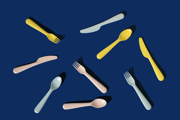 Set of plastic spoons, knives, forks on a blue background. Minimal horizontal flat lay composition, funny fast food serving concept - Foto, imagen