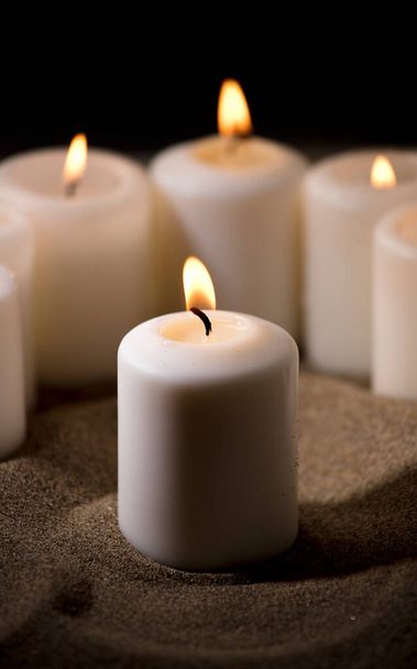 Концепция запугивания, составленная группой зажженных свечей, на песке с черным ночным фоном - Фото, изображение