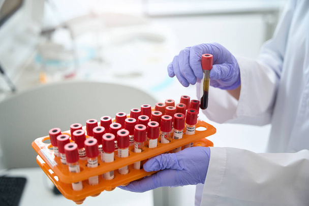 Photographie recadrée d'un assistant de laboratoire tenant des tubes préparés dans une banque de sang de machine de centrifugation de laboratoire - Photo, image