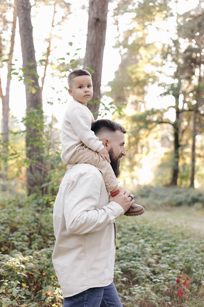 Father's day. Smiling dad holding his toddler son on shoulders look at camera outdoor at nature.Family spend and enjoy time together. Happy fatherhood and childhood, family love, togetherness concept. - Photo, image