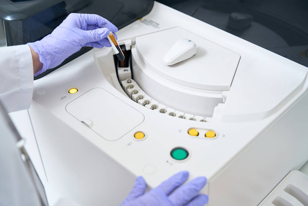 Сотрудник лаборатории отправляет образец крови на иммунохемилюминесцентный анализатор, это современное диагностическое устройство - Фото, изображение