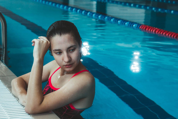 Young beautiful brunette girl on the background of the pool. Portrait of a girl near the side of the pool. Swimming, healthy lifestyle - Foto, Bild