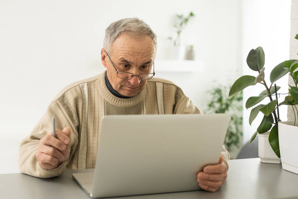 Knappe volwassen man in casual zitten in huis kantoor en werken op laptop. - Foto, afbeelding