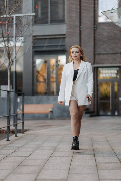 ブロンドスタイリッシュな女性で特大ホワイトジャケット上の街の背景 - 写真・画像