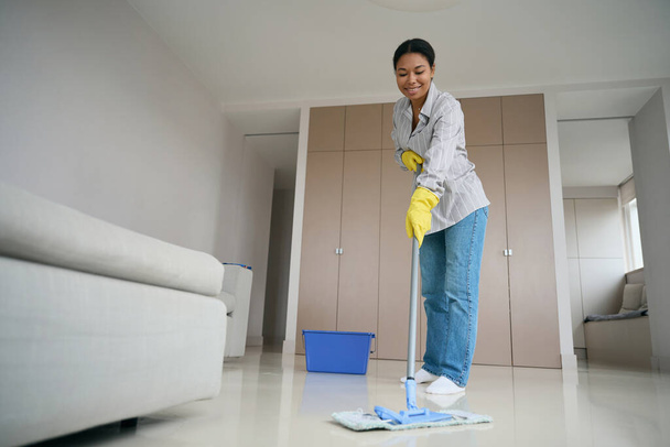 Smiling emale african american mopping the floor in the living room, woman in comfortable casual clothes - Fotoğraf, Görsel